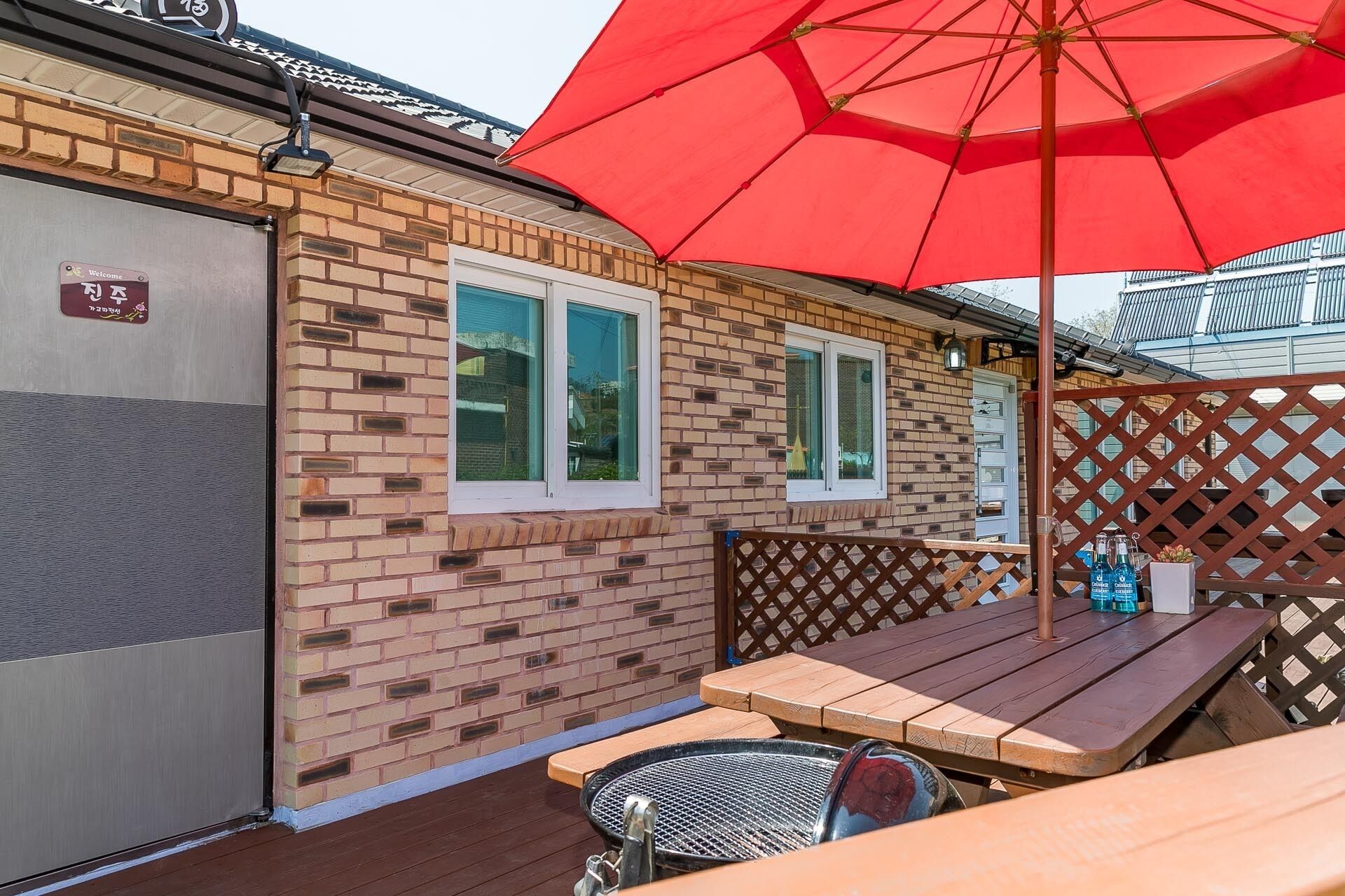 Una casa de ladrillo con una puerta de garaje, una terraza de madera y un paraguas rojo.