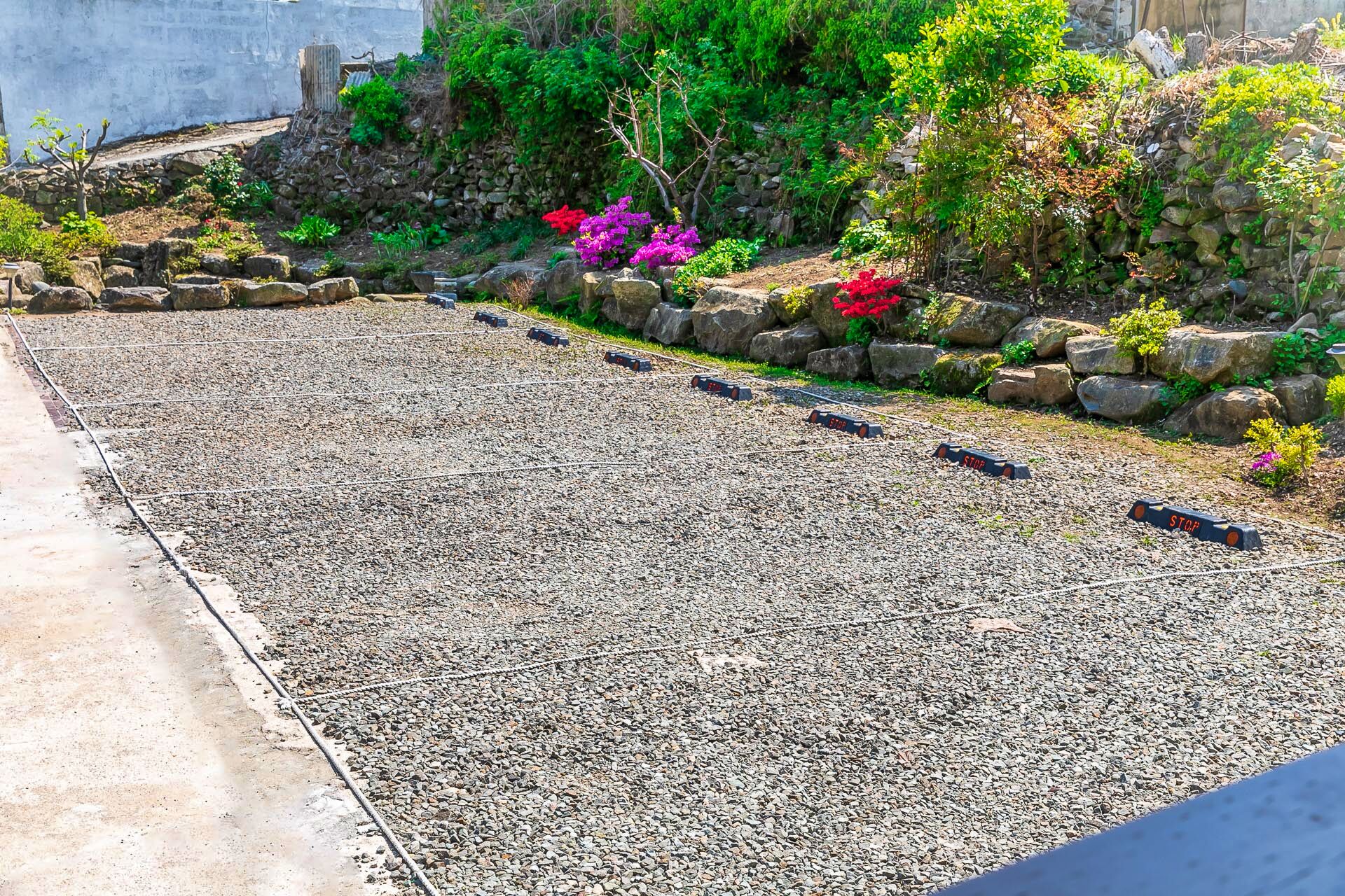 Um jardim com caminho de cascalho, muros de pedra e diversas plantas.
