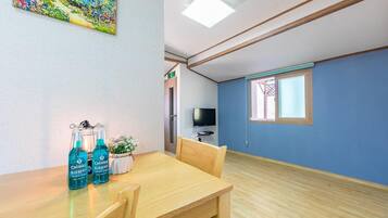 A room with a wooden table, two bottles of blue beverage, a small plant, and a television on a stand.