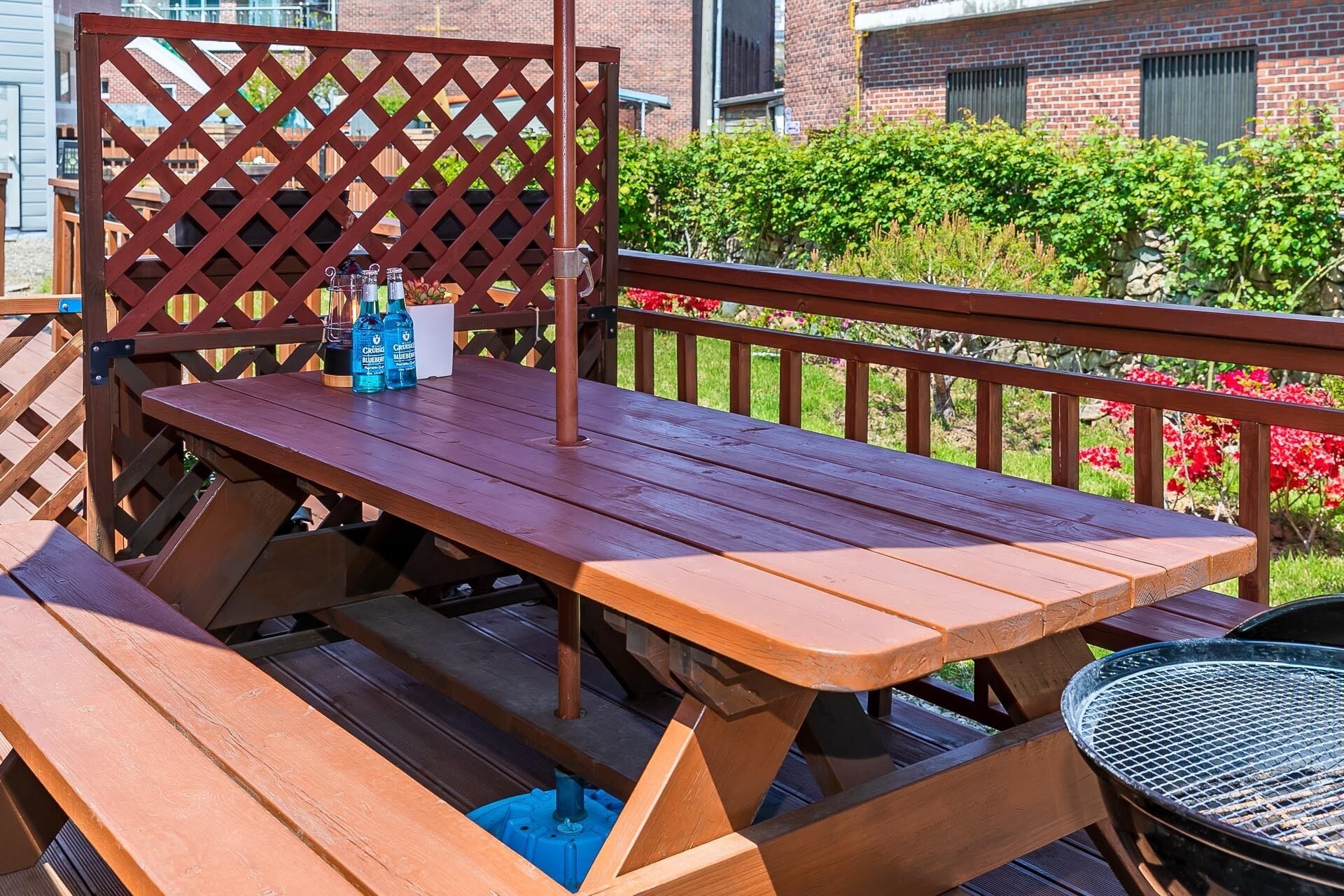 Una mesa de picnic de madera con bancos, una parrilla de metal y una valla de celosía.