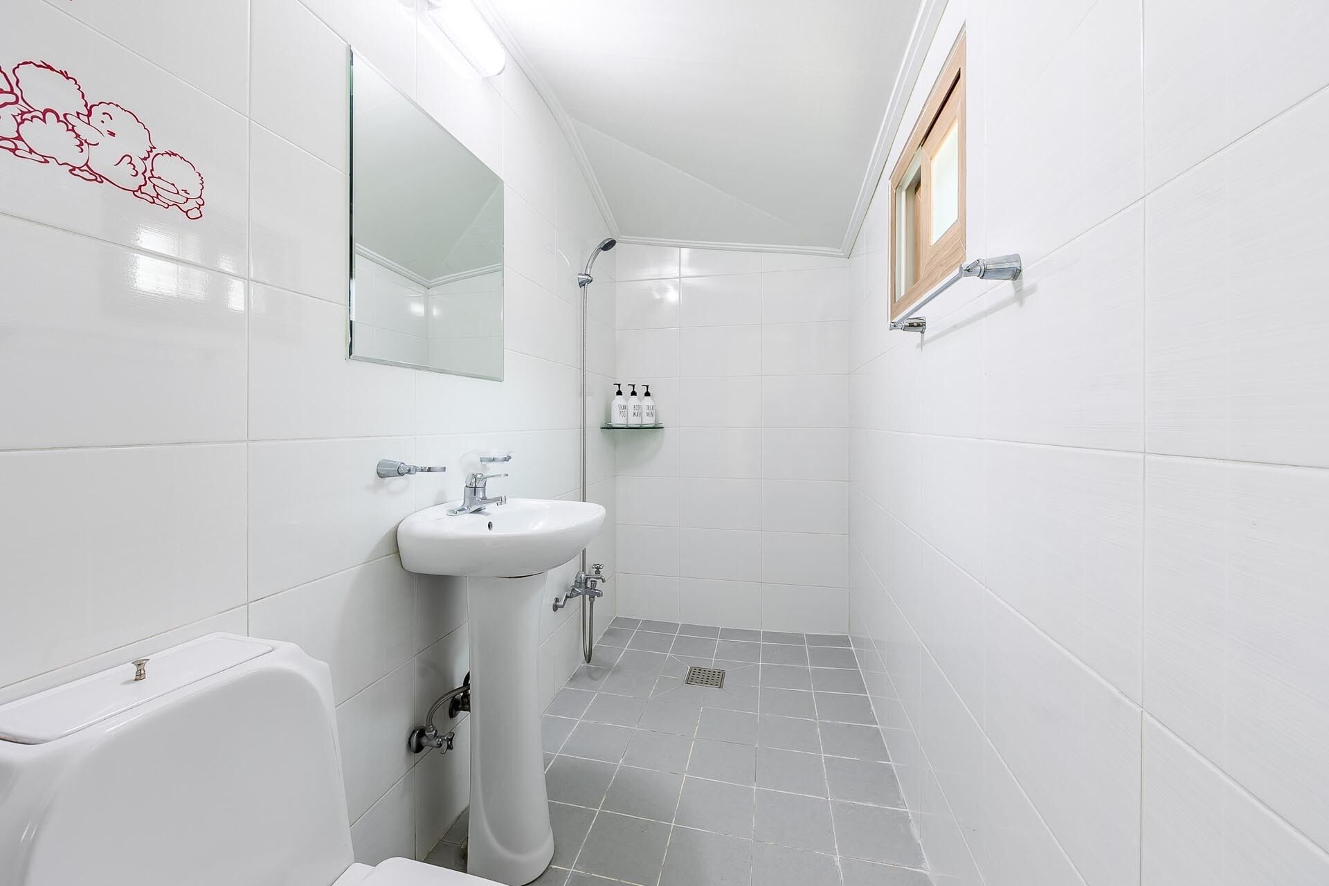 A small, modern bathroom with white tiles, a pedestal sink, a toilet, and a shower.