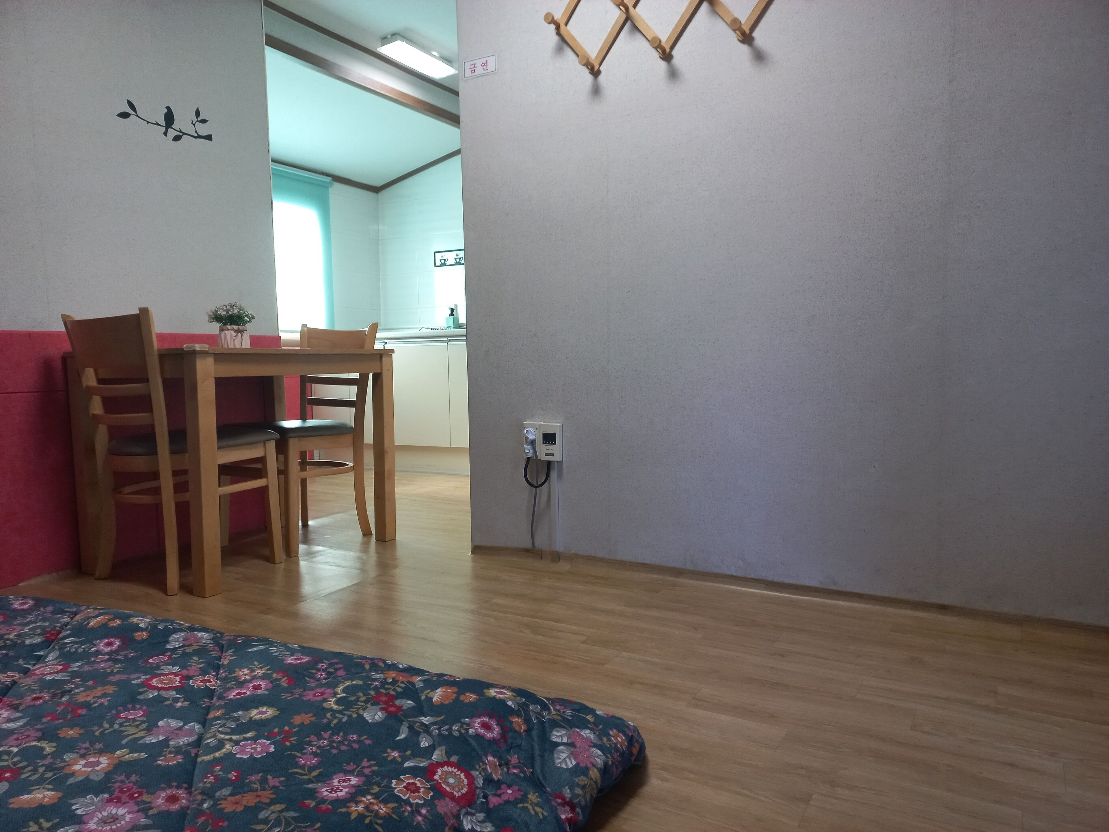 A room with a bed, a dining table with chairs, a wall-mounted light fixture, and a power outlet.
