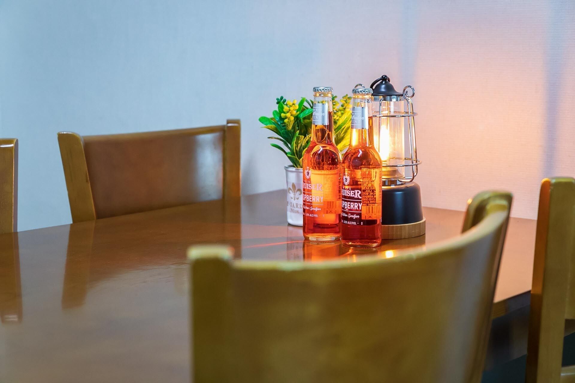Een houten eettafel met twee flessen 'Cruiser' en een glazen lantaarn.