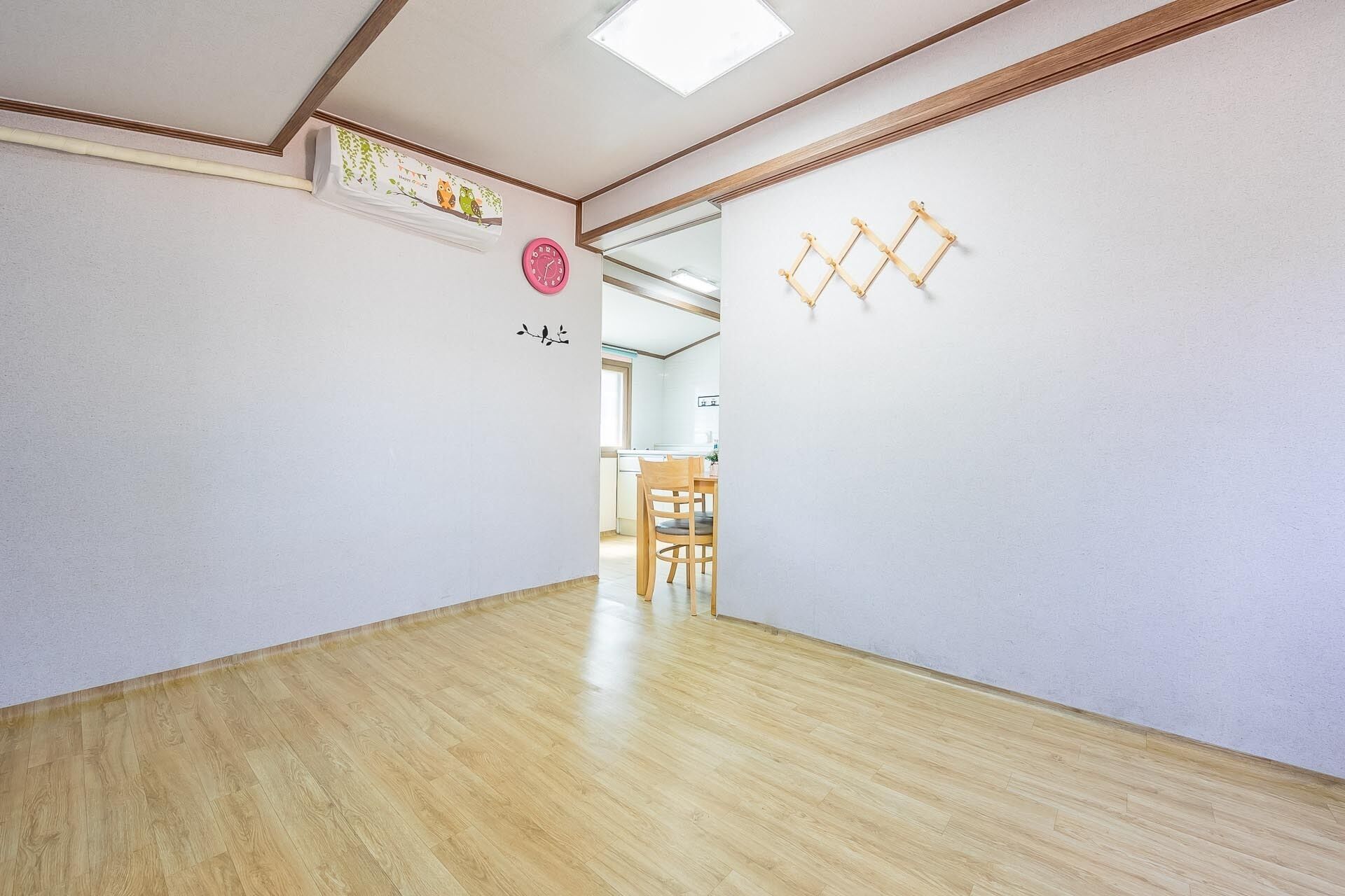 A hallway with wooden flooring, white walls, a ceiling with recessed lighting, and a door leading to a room with a dining table and chairs.