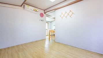 A hallway with wooden flooring, white walls, a ceiling with recessed lighting, and a door leading to a room with a dining table and chairs.