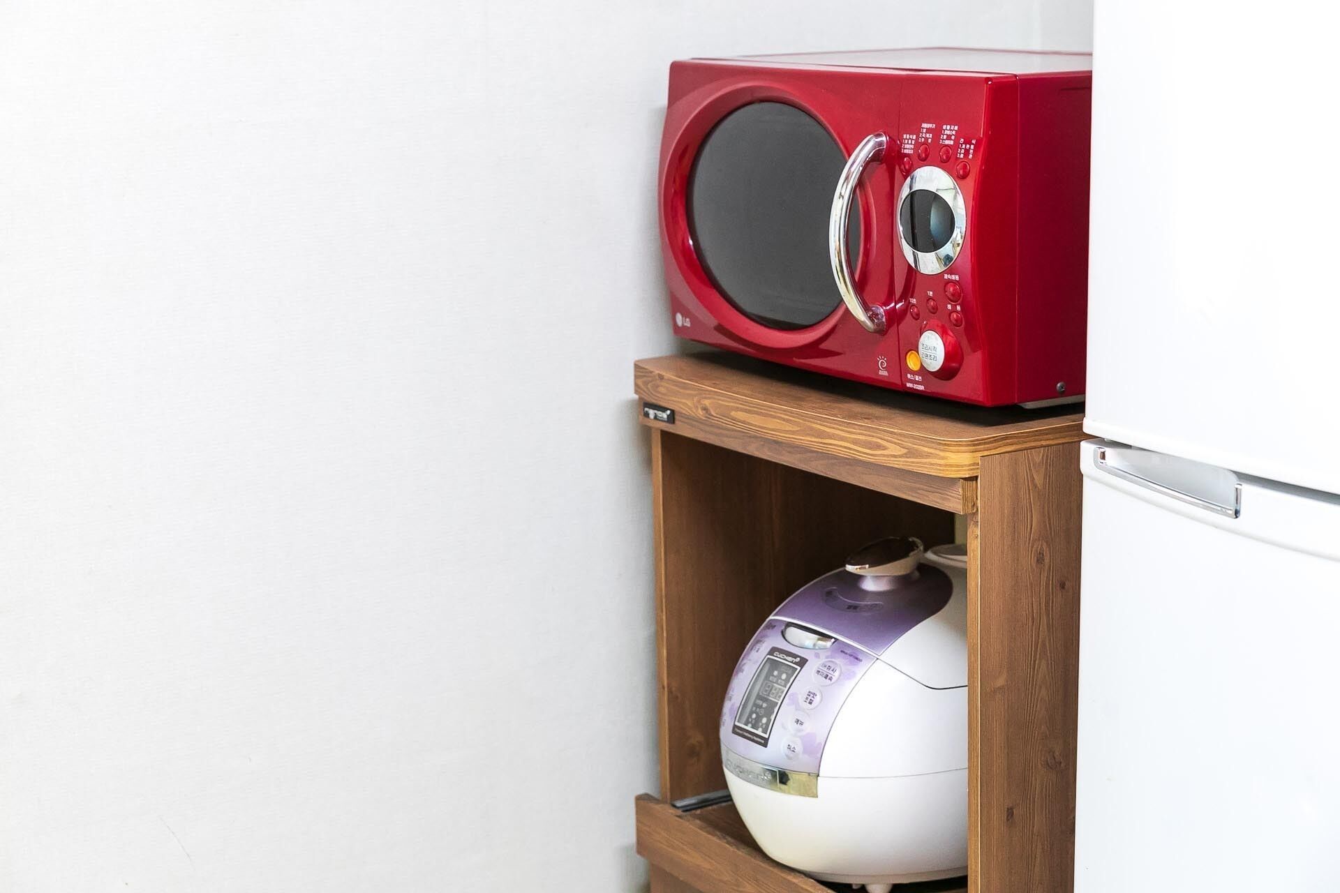 A microwave on a wooden shelf above a rice cooker.