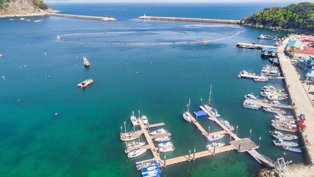Un puerto deportivo con barcos amarrados a muelles de madera, rodeado de aguas azules cristalinas y un paisaje montañoso.