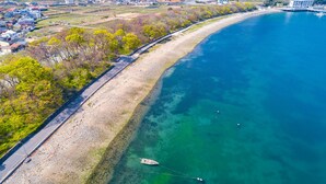 Vista aérea de una zona costera con una playa despejada, una carretera paralela a la orilla y un barco anclado en el agua.