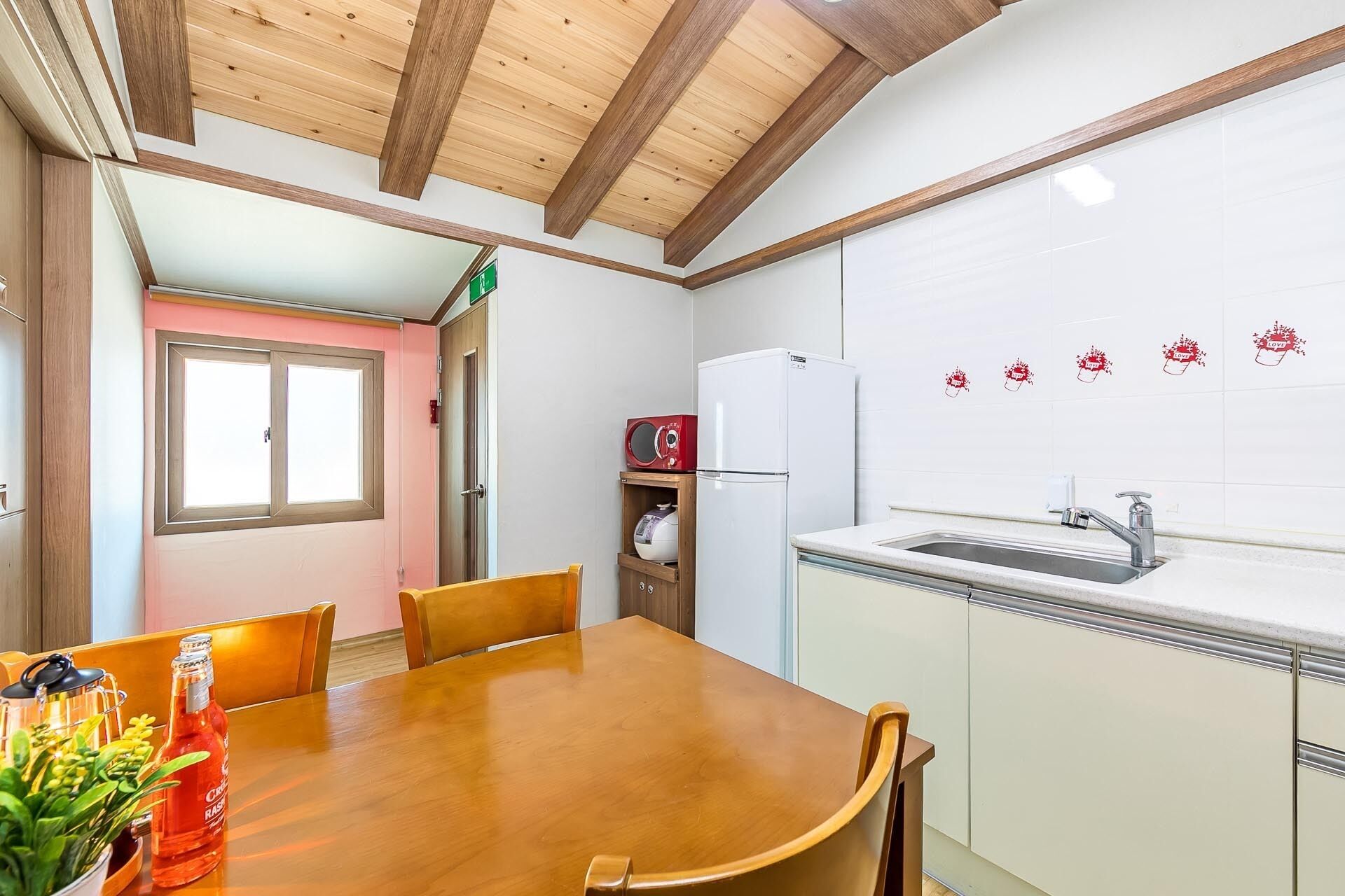 A kitchen with a wooden table, chairs, a refrigerator, a microwave, and a sink.