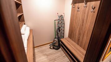 Una habitación de hotel pequeña con un armario de madera, una cama con ropa blanca y un aspirador en la esquina.