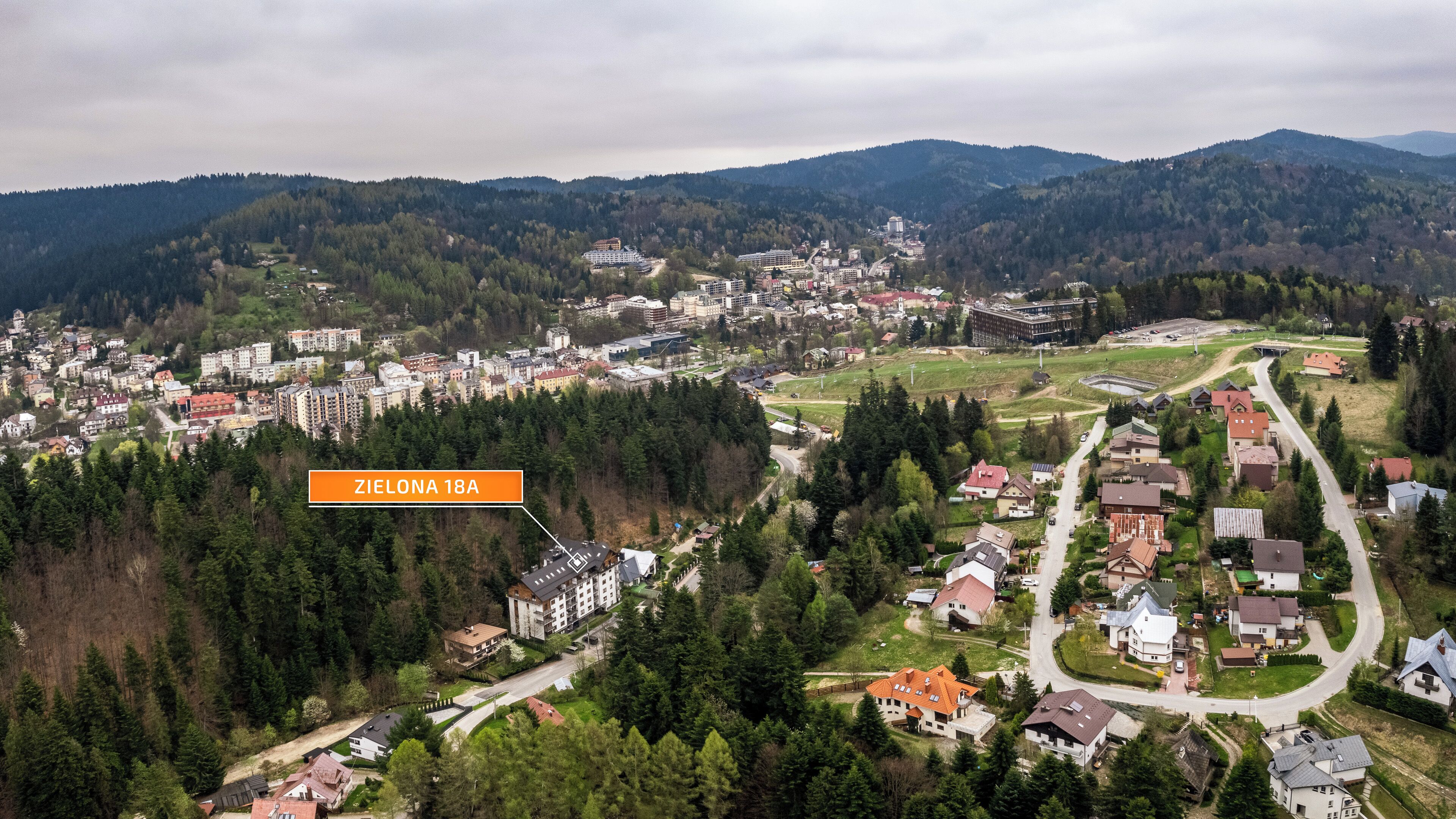 An aerial view of a town with a mix of residential and commercial buildings, surrounded by forested hills.