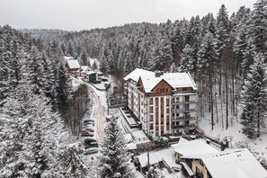A multi-story building surrounded by snow-covered trees, likely a hotel or resort. - Apartamenty Sun & Snow Zielony Las (Krynica-Zdroj)