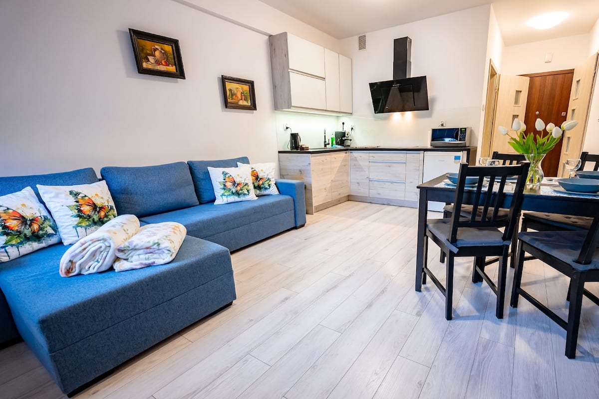 Un salon moderne avec un canapé bleu, une table à manger avec des chaises et, au fond, un coin cuisine.