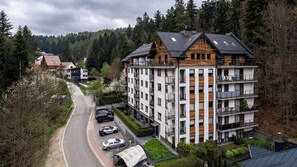 A multi-story residential building with balconies, a parking area, and a road leading to it.