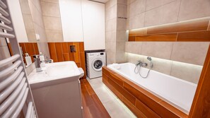 A modern bathroom with a sink, washing machine, and a large bathtub.