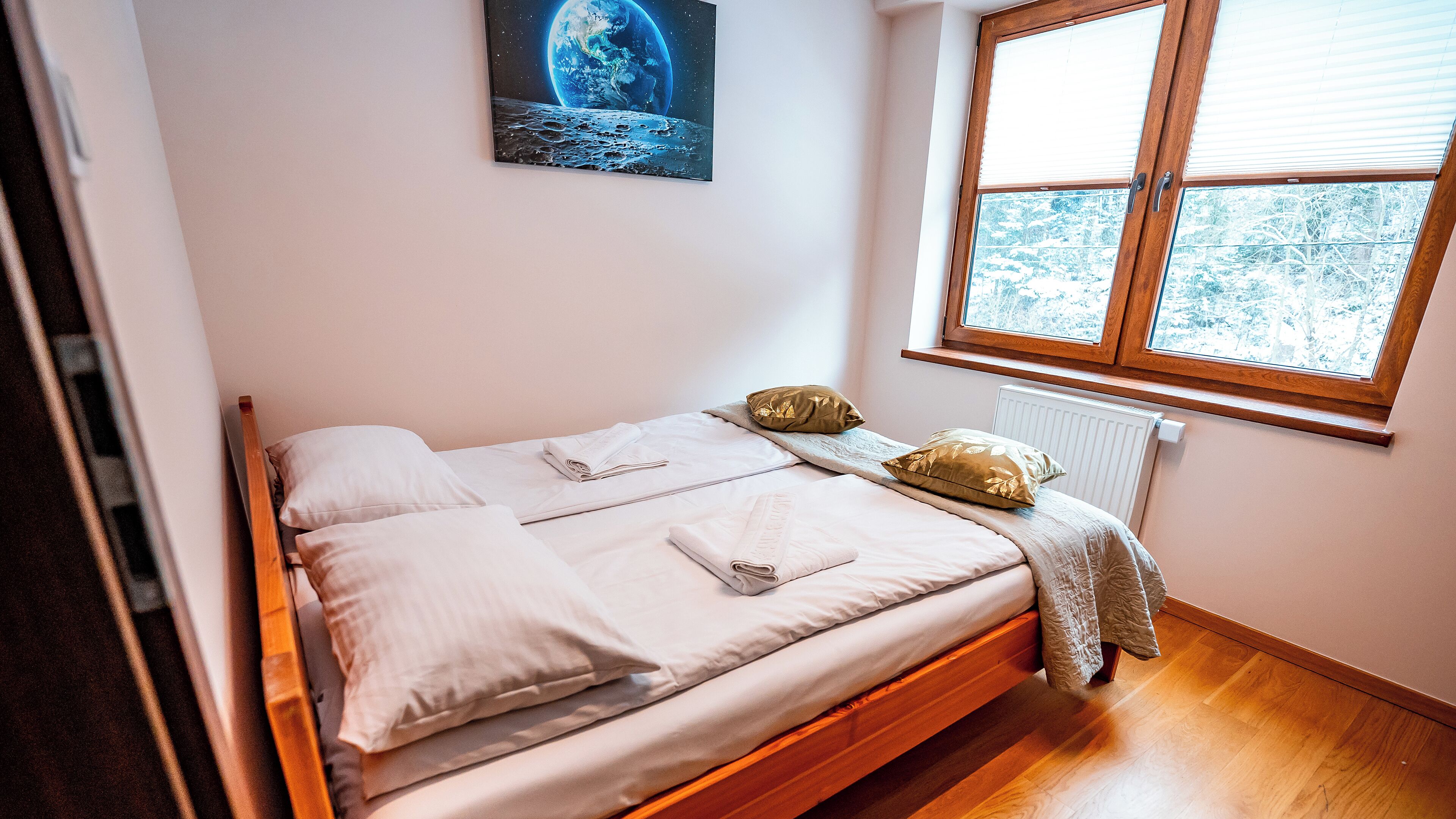 Un lit bien fait, avec du linge de lit blanc et des coussins dorés, une tête de lit en bois et une fenêtre donnant sur les arbres.