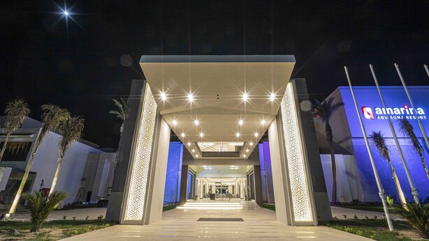 A modern hotel entrance with a geometric facade, a central atrium, and palm trees.