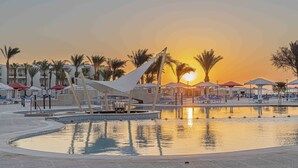A resort pool area with palm trees, lounge chairs, and umbrellas during sunset.