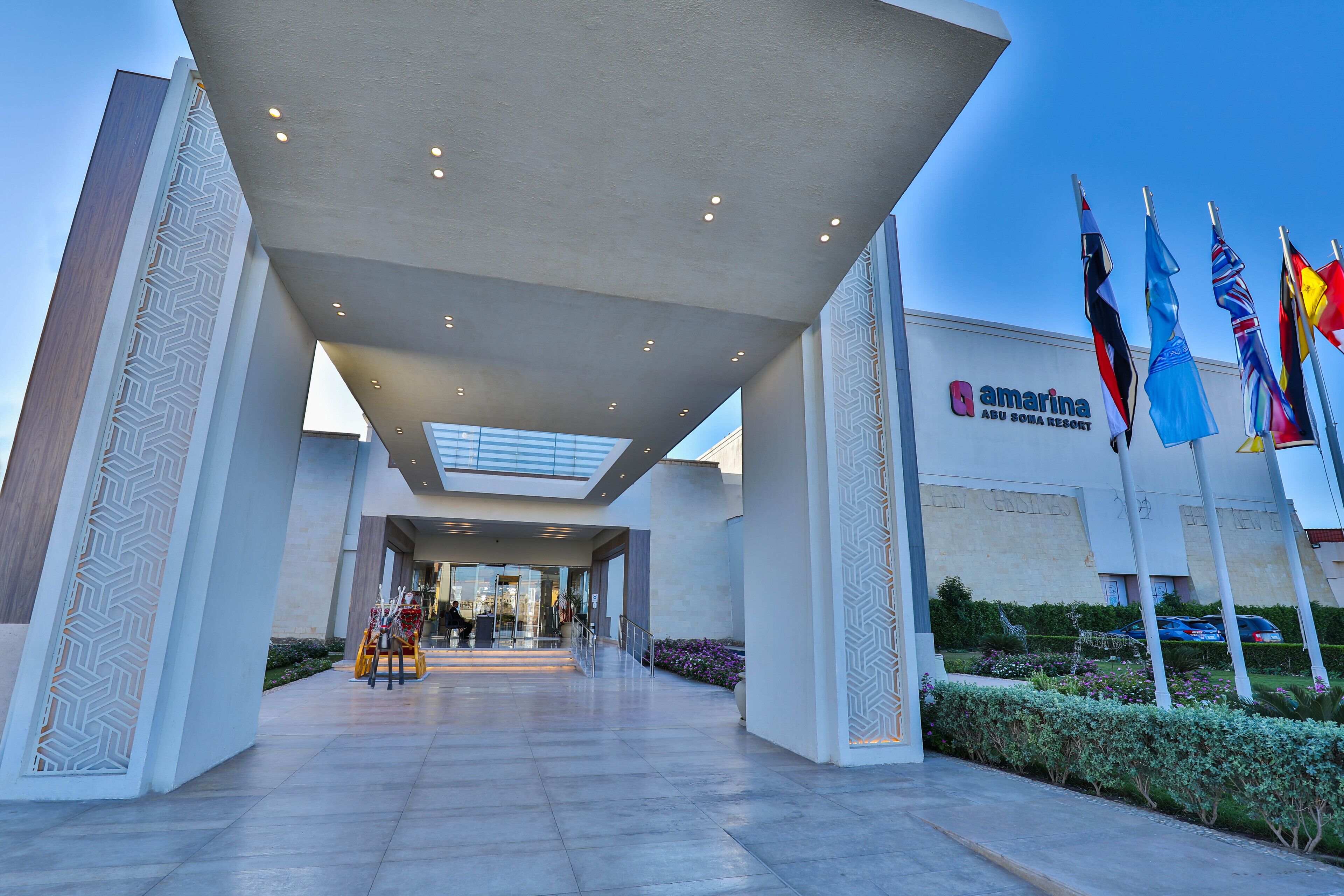 A modern hotel entrance with a geometric facade, a clear sky, and multiple flags.