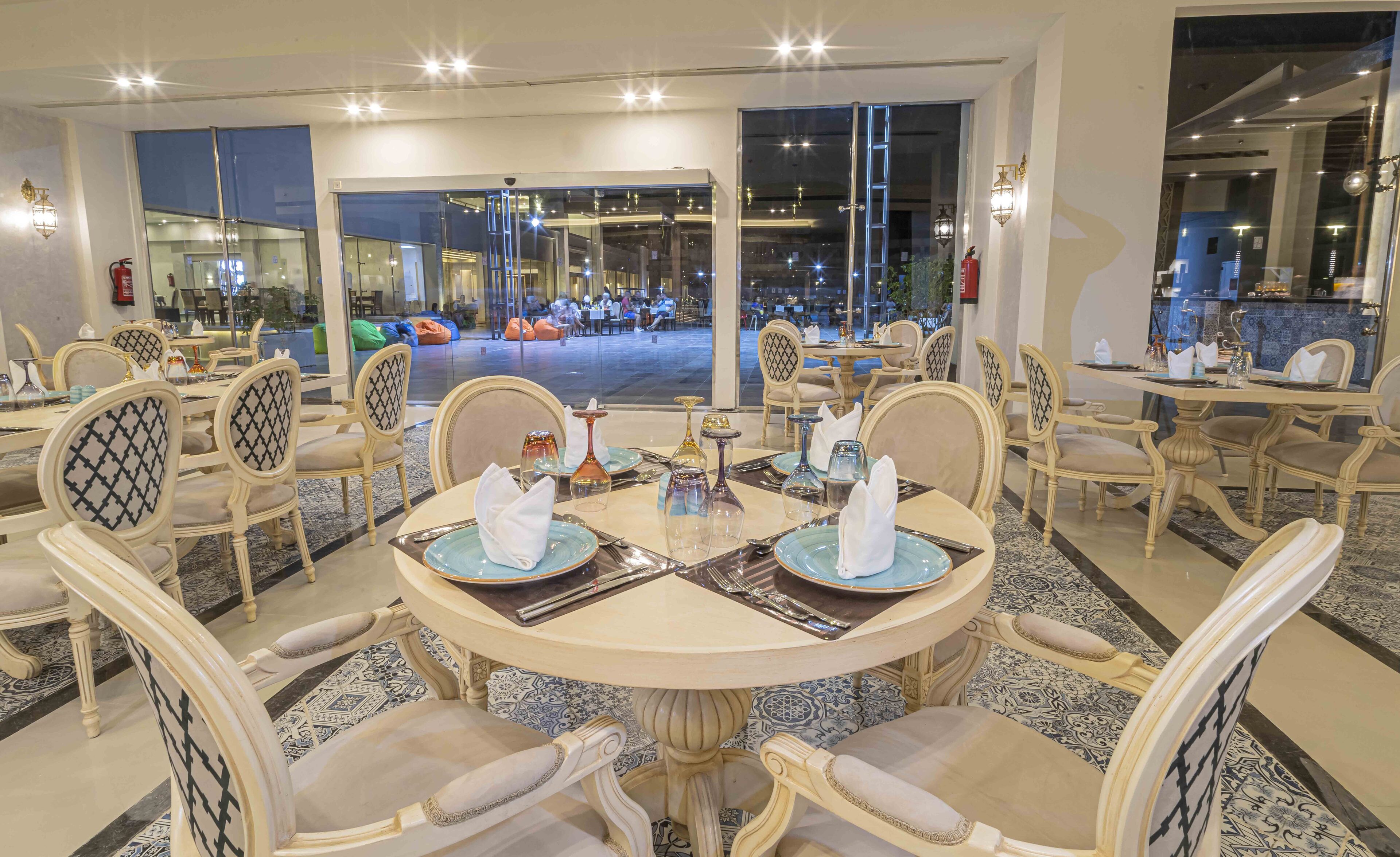 A dining area with round tables, chairs, and a view of the outdoor seating area.