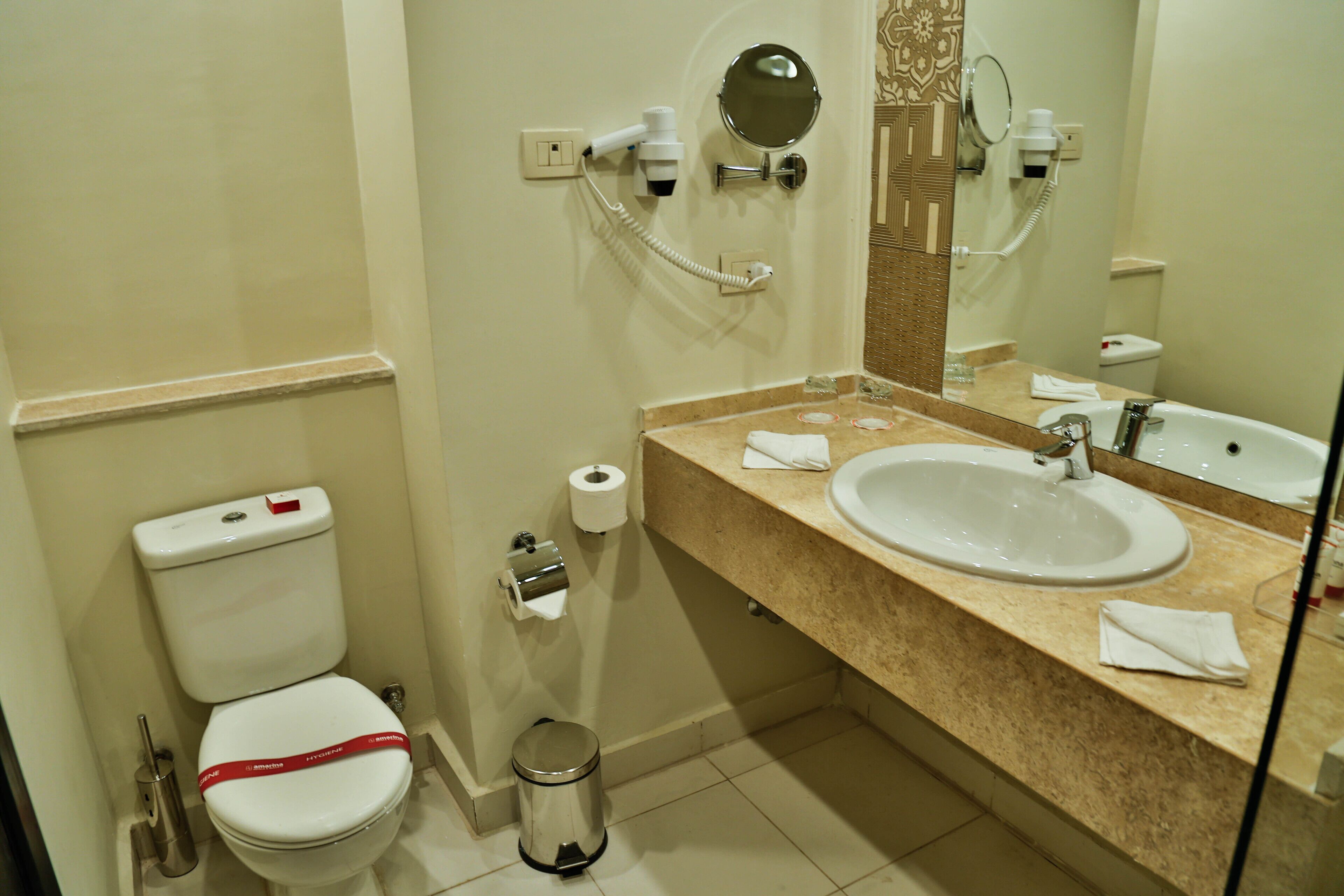 Baño con inodoro, lavabo, espejo y dispensador de toallas.