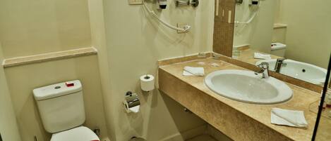 Baño con inodoro, lavabo, espejo y dispensador de toallas.