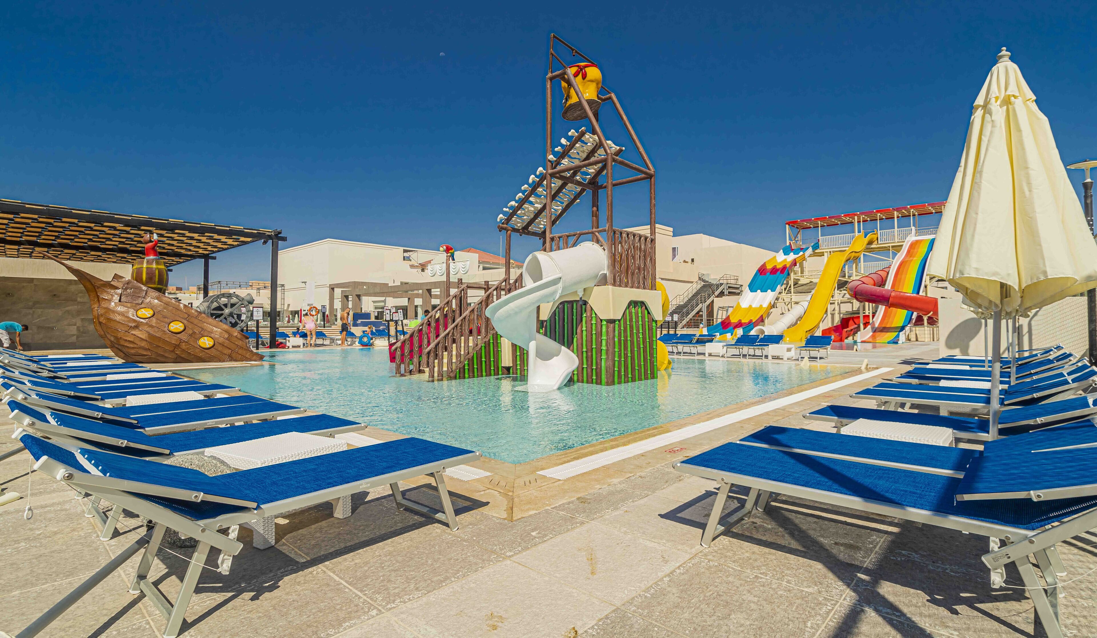 A pool area with water slides, lounge chairs, and a lifeguard stand.