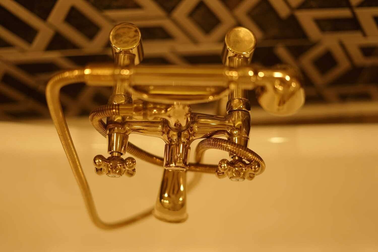 A metallic faucet with three separate spouts and a flexible hose, likely part of a bathroom fixture.