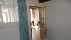 A bedroom with a bed, a wooden door, and a view into another room.