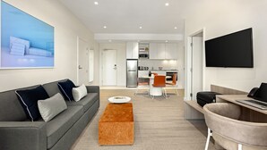 Ein modernes Wohnzimmer mit einem grauen Sofa, einem braunen Hocker und einem flachbildfernseher an der Wand.
