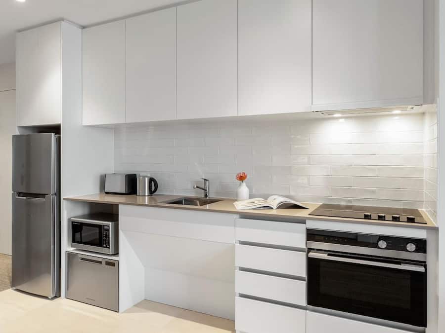 A modern kitchen with white cabinetry, a stainless steel refrigerator, a microwave, a sink, and a built-in oven.