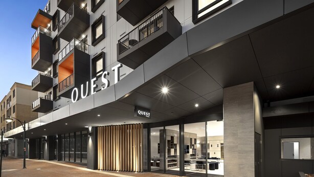 Ein modernes Hotel mit einem gut sichtbaren 'QUEST'-Schild, großen Fenstern und einem klaren, zeitgemäßen Design.