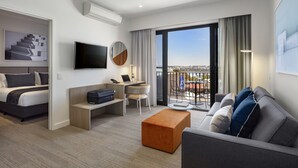 Ein modernes Hotelzimmer mit Bett, Schreibtisch, einer Couch, einem Fernseher und einem Balkon mit Blick auf die Stadt.