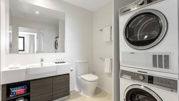 A modern bathroom with a double sink, toilet, and stacked washer-dryer unit.