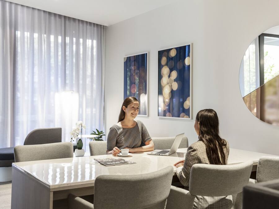 A modern meeting room with a glass table, grey upholstered chairs, and abstract wall art.