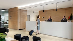 Ein moderner Hotel-Empfangsbereich mit einem Holzbüro, schwarzen Stühlen und einer Wartezone mit Tisch und Sitzgelegenheiten.