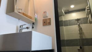 Ein Badezimmer mit einem weißen Waschbecken, einem Spiegel, einem Handtuchhalter und einer Duschkabine mit gefliesten Wänden.