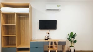 Ein Zimmer mit Holzschrank, Schreibtisch mit Stuhl, Flachbildfernseher und einer Topfpflanze.
