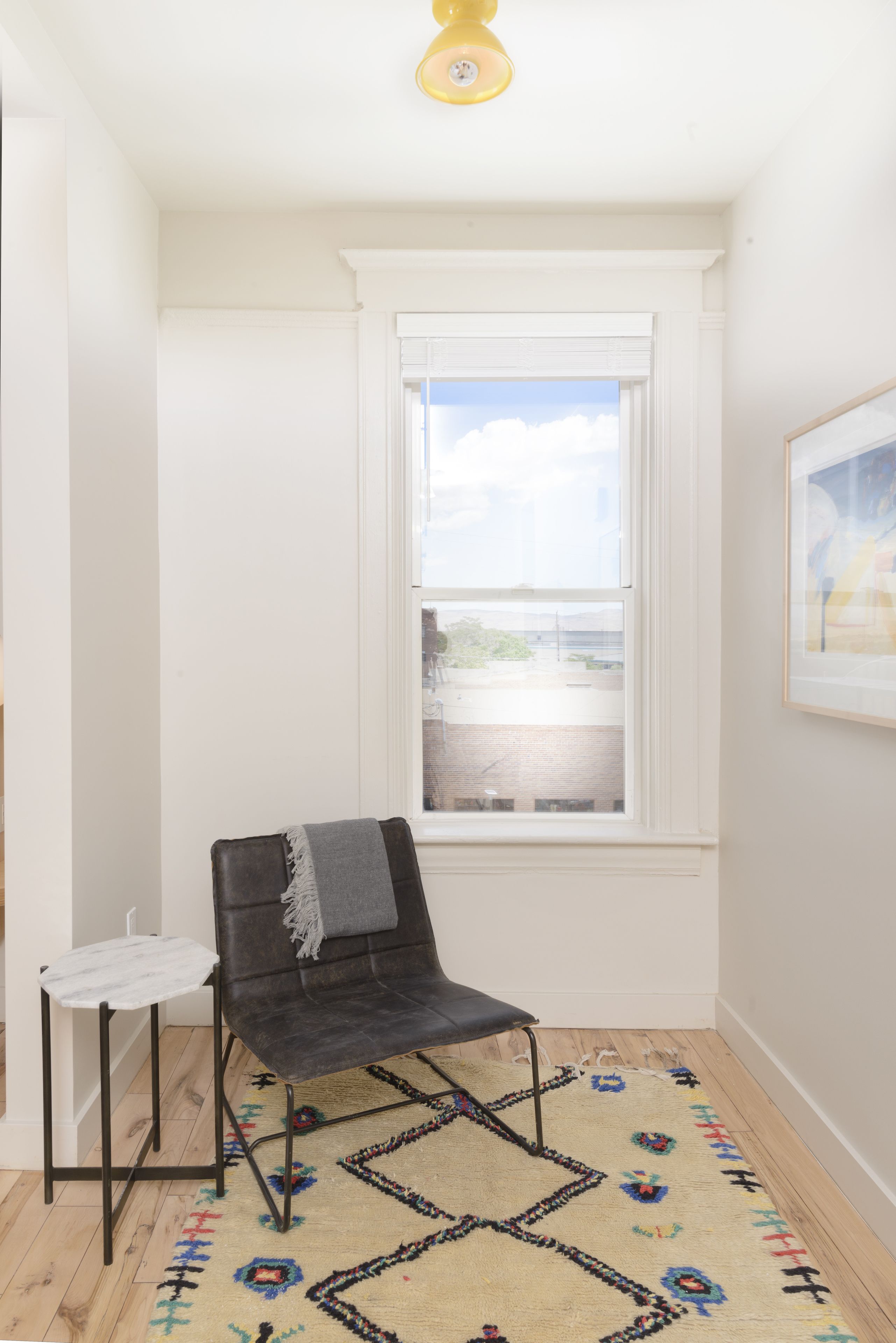A corner room with a black chair, a small white table, and a patterned rug.
