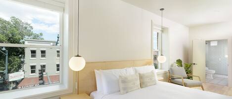 A modern bedroom with a large bed, bedside tables, a chair, and a view of the city through a window.