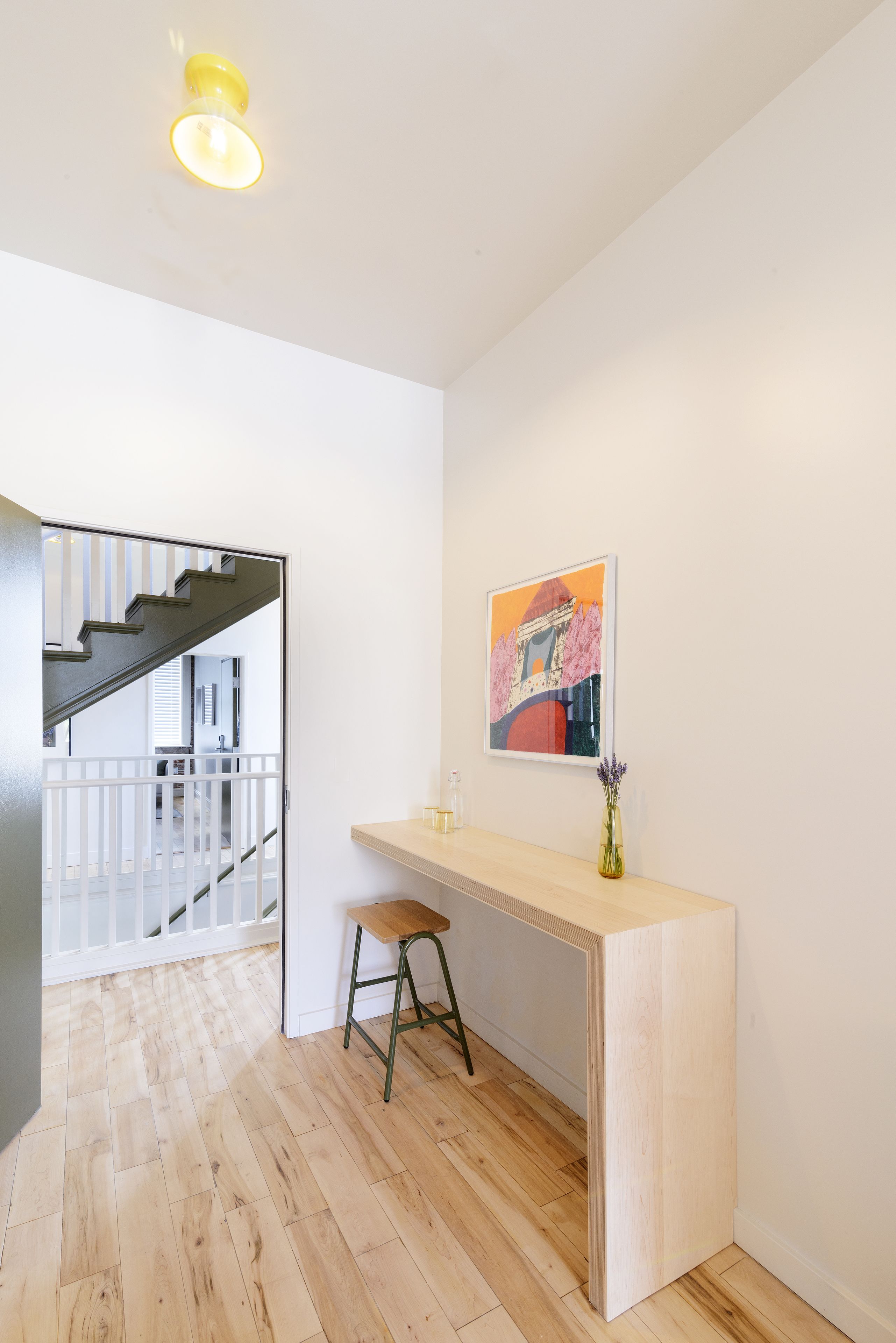 A modern kitchen with a wooden countertop, a stool, and a framed artwork on the wall.