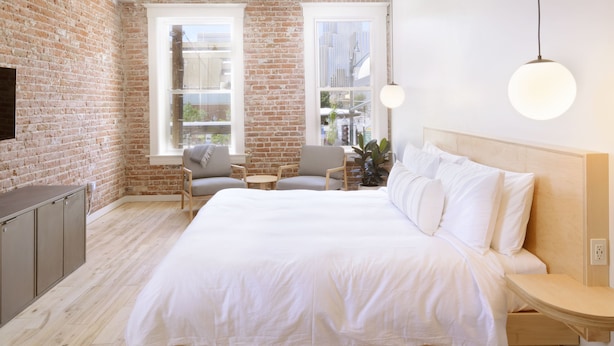 A modern bedroom with a large bed, a brick wall, and a view of the city. - The Jesse Hotel & Bar (Reno)