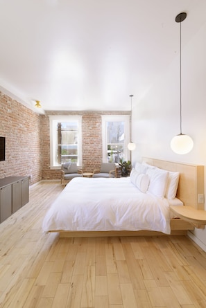 A modern bedroom with a large bed, a brick wall, and a view of the city. - The Jesse Hotel & Bar (Reno)