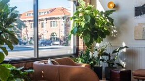 A cozy room with a large window, a brown leather sofa, and several small round tables. - The Jesse Hotel & Bar (Reno)