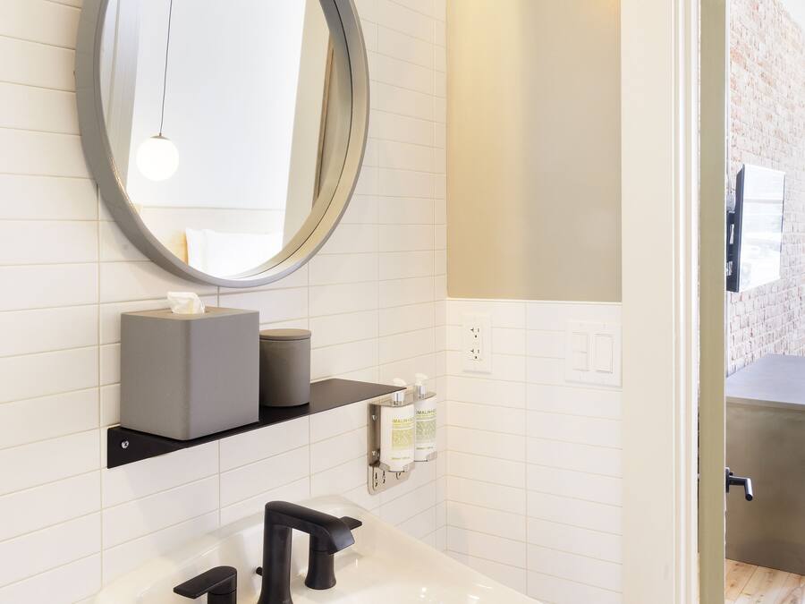 A bathroom with a white sink, a round mirror, and a yellow light fixture.