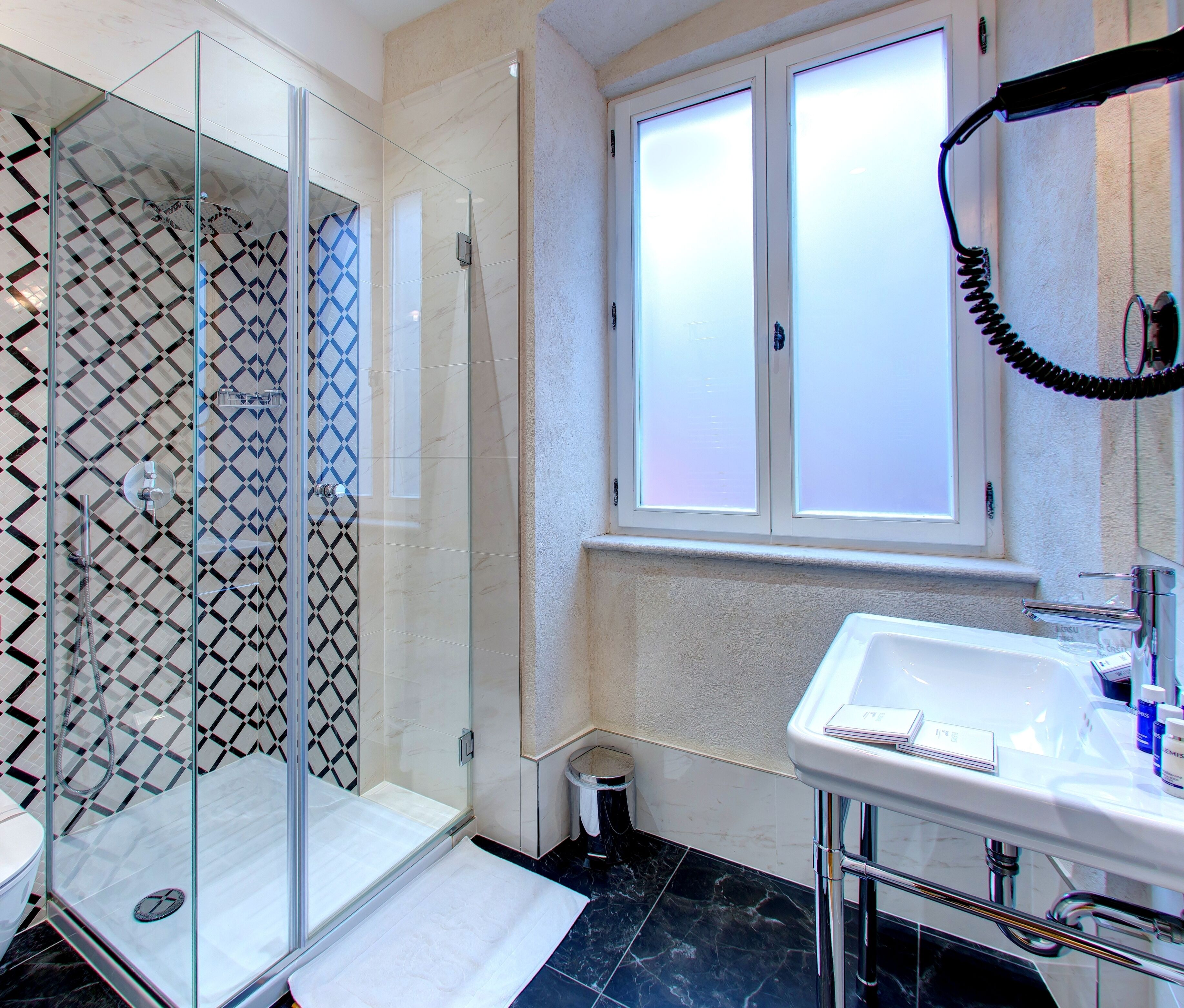 Un bagno moderno con doccia vetrata, lavandino bianco e finestra con vetro satinato.