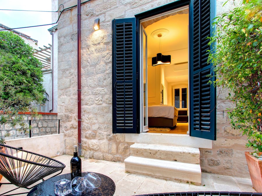 Un bâtiment en pierre dont on aperçoit une chambre à coucher à travers des volets ouverts.