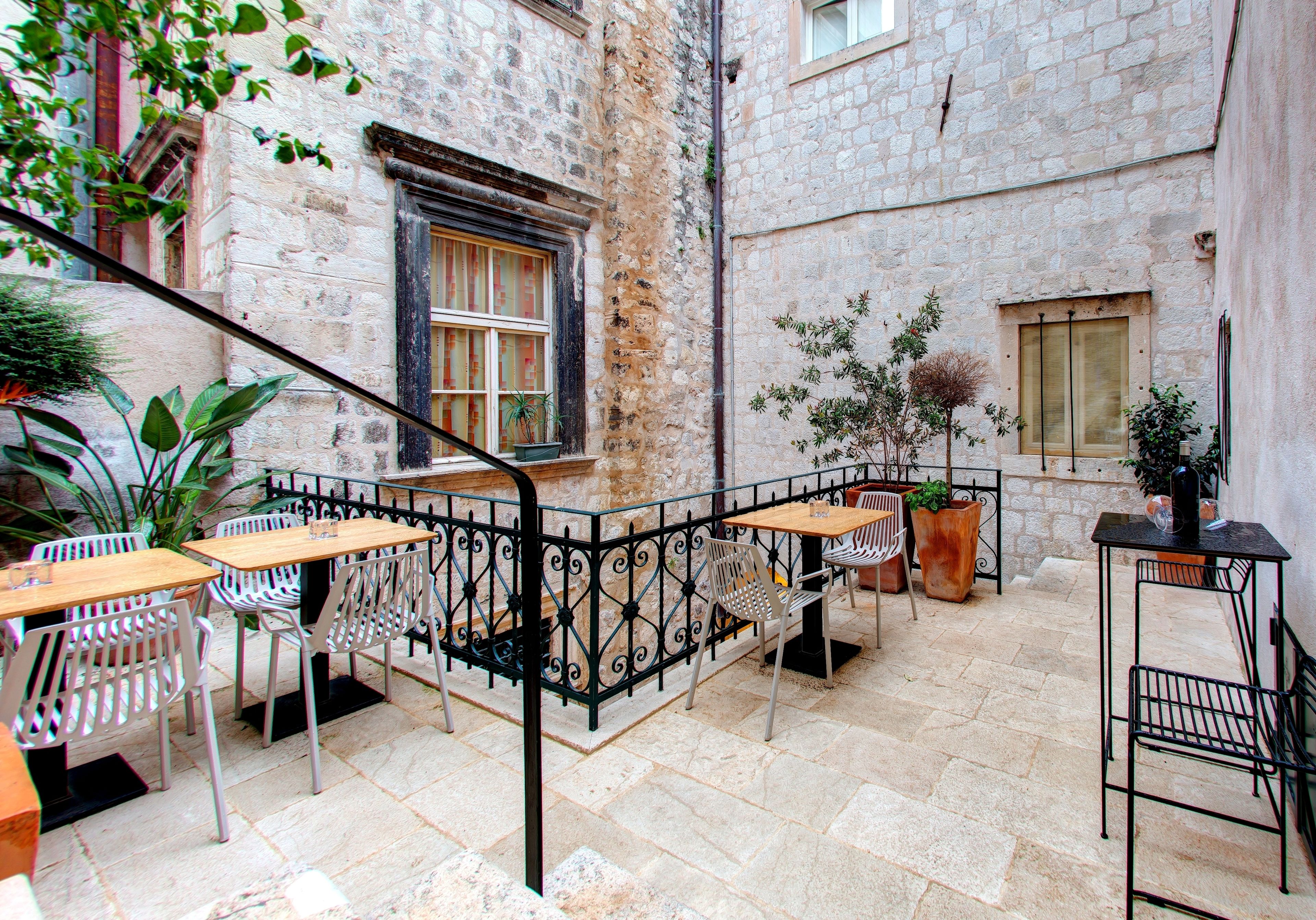 An outdoor café with stone walls, metal furniture, and potted plants.