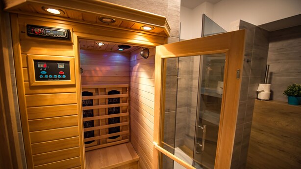 Uma sauna com painel de controle, bancos de madeira e área de chuveiro em vidro.