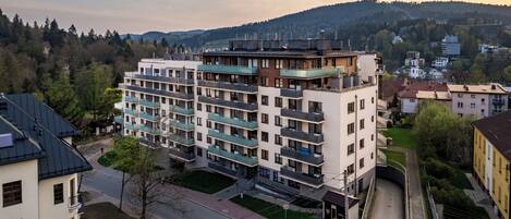 A multi-story residential building with balconies, a central courtyard, and a view of surrounding hills.